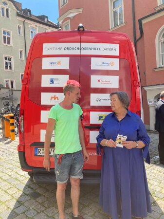 Vorstandsvorsitzende der Stiftung Johanna Rumschöttel im Gespräch mit dem zukunftigen Fahrer des NOAH-Mobil Streetworker Ben Peter vor dem NOAH-Mobil des Caritasverband stehend
