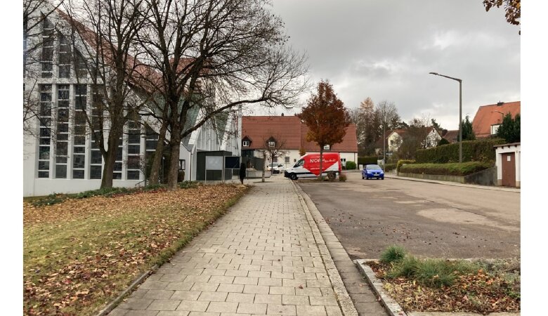NOAH-Mobil steht auf einem Parkplatz vor einer Kirche im Hintergrund sind Häuser zu sehen und ein blaues Auto