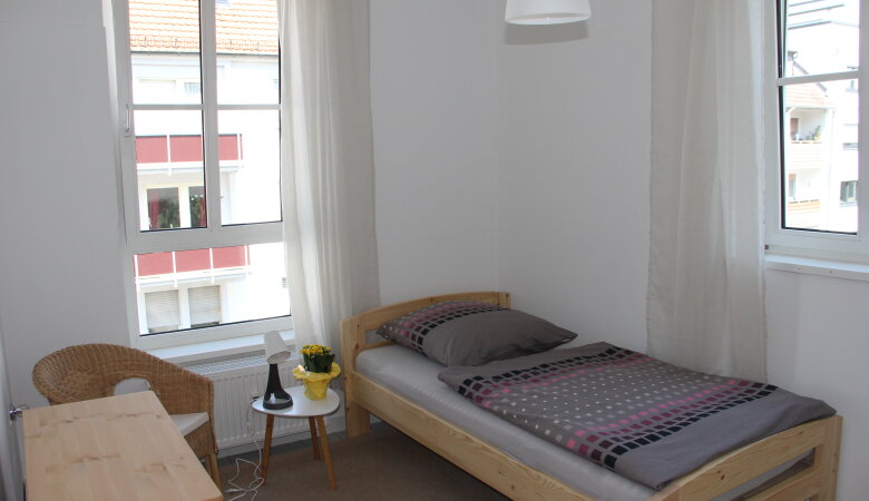 Schlafraum mit Bett, Tisch, Stuhl und Fenstern