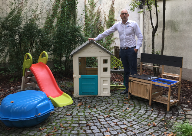 Person steht neben Gartenspielhaus, Rutsche, Sandkasten, Bank